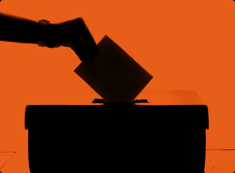 A hand posts a folded ballot into a ballot box.